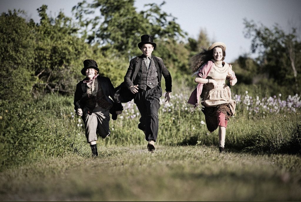 Trois enfants en costume courent à travers un champ.