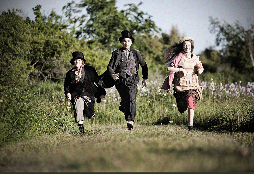 Three children running through a field in costume.