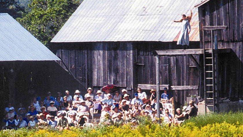 Assis à l’extérieur, l’auditoire lève les yeux pour regarder un acteur qui joue sur une scène surélevée à côté d'une grange.