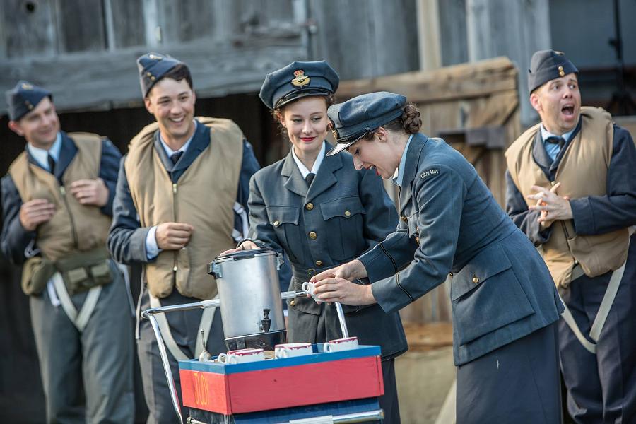 Des acteurs et des actrices en uniforme de l'Aviation royale canadienne à l’époque de la Seconde Guerre mondiale plaisantent près d’un chariot à café dans la pièce Bombers: Reaping the Whirlwind, produite par 4th Line Theatre.