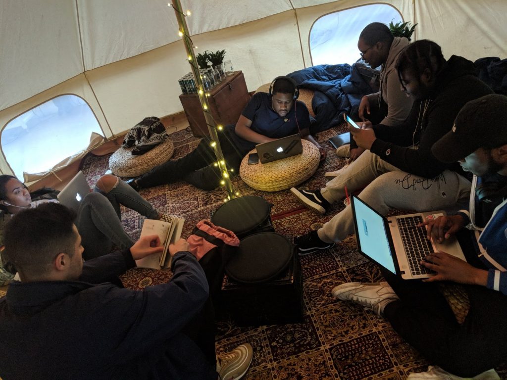 The Remix Project participants sit around on the floor working on laptops.