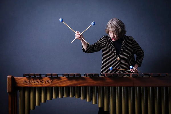 Personne jouant du marimba avec quatre maillets, un bras levé en pleine performance.