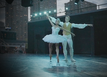 Two ballet dancers performing on an outdoor stage.