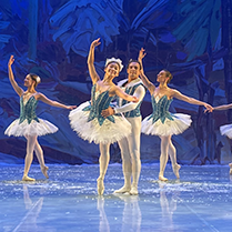 Ballet dancers perform on a stage with a blue backdrop.