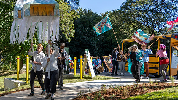 Des personnes défilent avec de grandes marionnettes et des drapeaux.