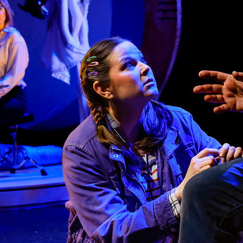 A girl crouches on a stage looking up.