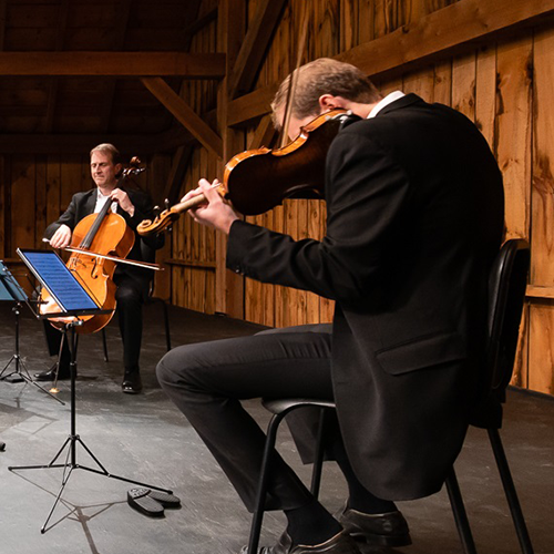 Deux hommes assis face à face sur une scène jouent des instruments à cordes.