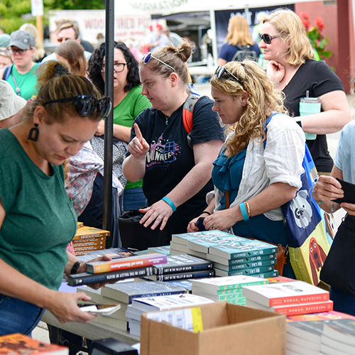 Visitors peruse stacks of books displayed for sale at outdoor stands.